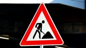 A triangular road sign with a red border, with a black stick man holding a pole which is digging into a triangle which represents building materials.